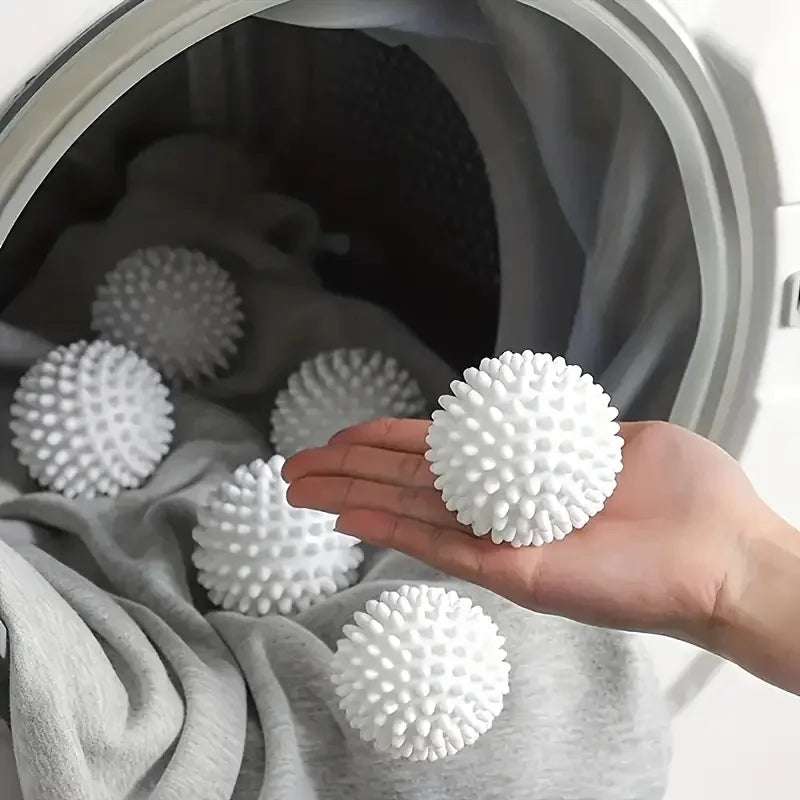 Hand holding a white, spiked laundry dryer ball in front of an open washing machine drum containing more balls.
