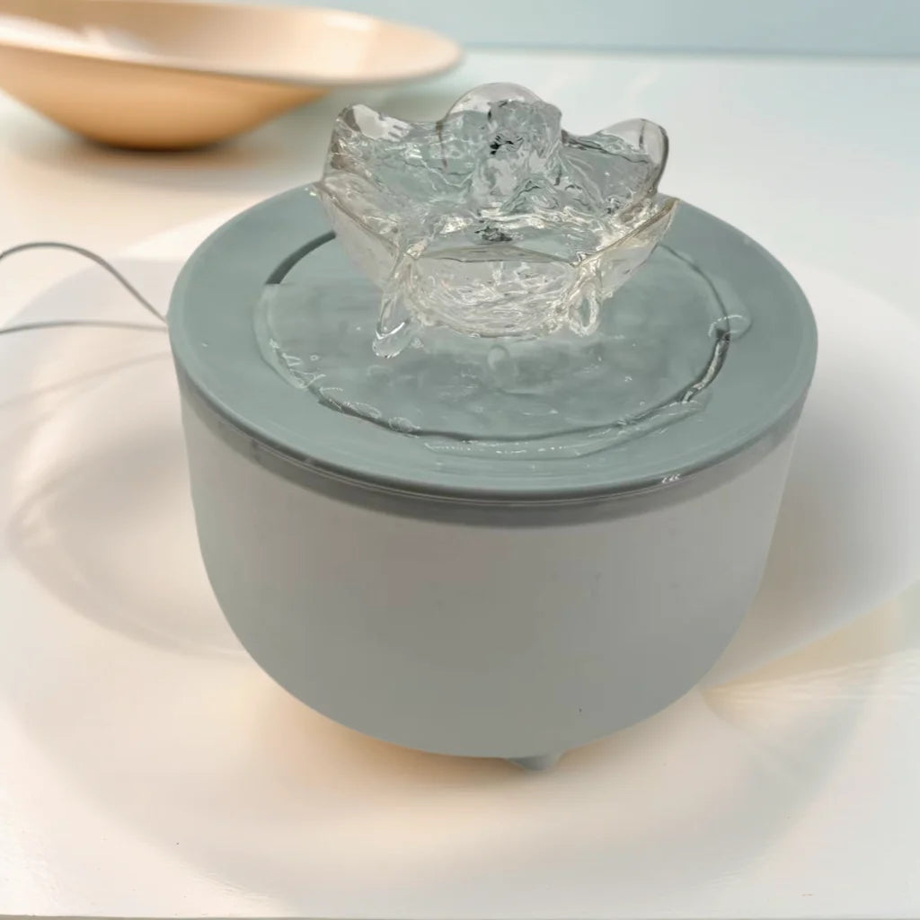 A minimalist, light gray cylindrical pet water fountain with a clear flower-shaped spout.