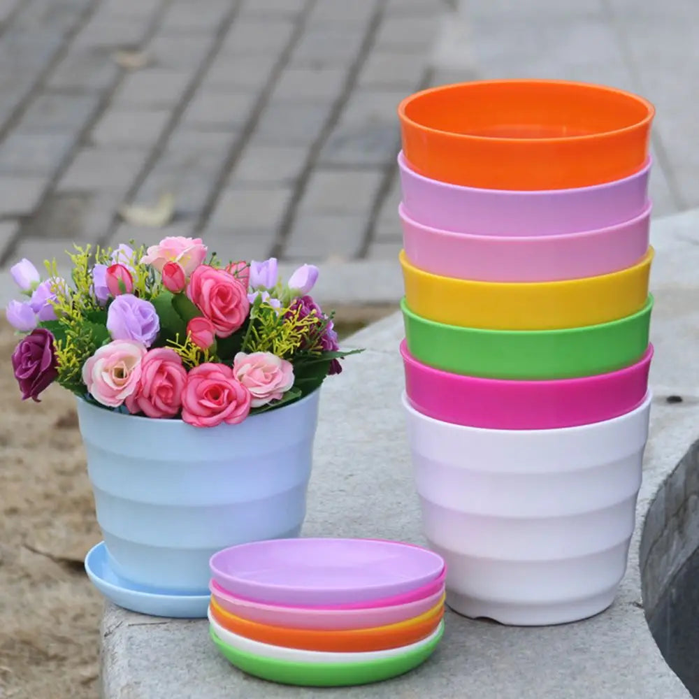 A stack of colorful plastic flower pots, a single pot with faux flowers, and a stack of matching saucers.