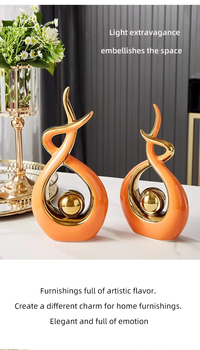 Two modern, orange and gold ceramic abstract sculptures standing on a white table.