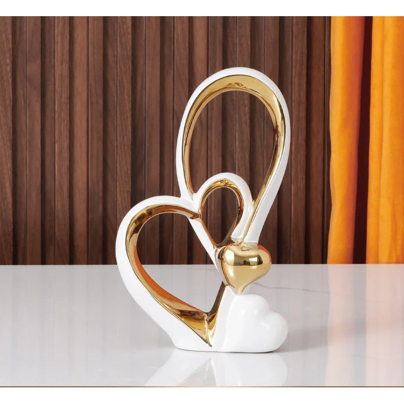 Minimalist white and gold ceramic ornament featuring elegant, interlocking heart-shaped silhouettes.