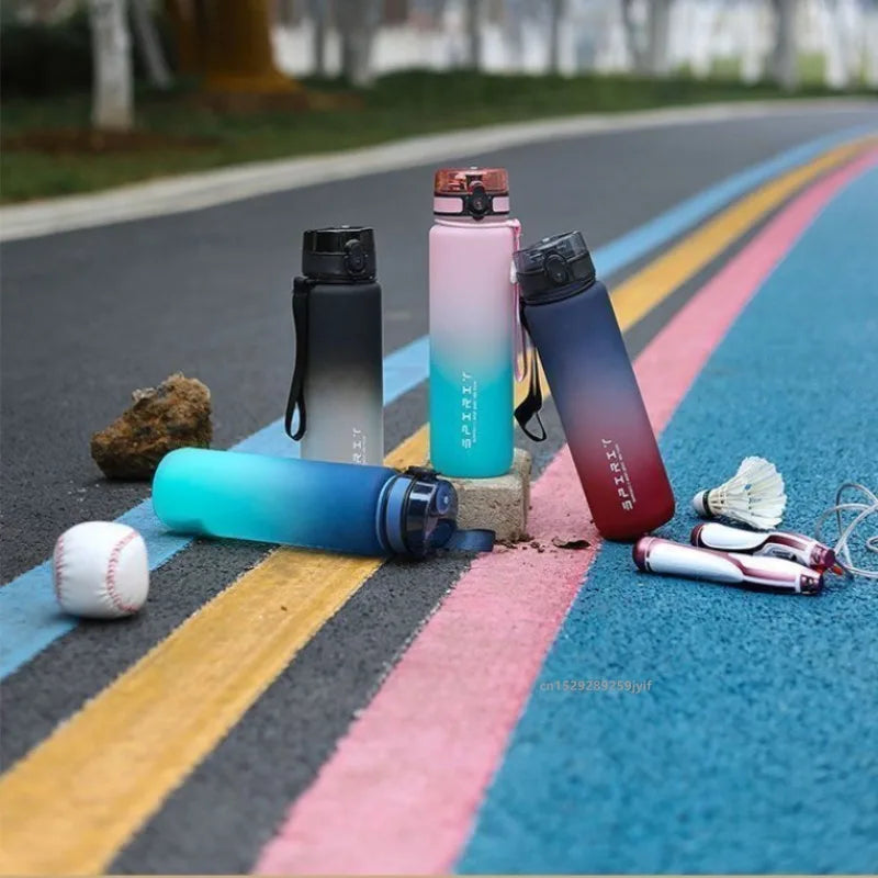 Four colourful ombre sports water bottles with flip-tops, labelled "SPIRIT", arranged on a multi-coloured track.