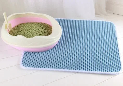 Blue honeycombed double-layer waterproof cat litter mat next to a pink and white litter tray on a white floor.