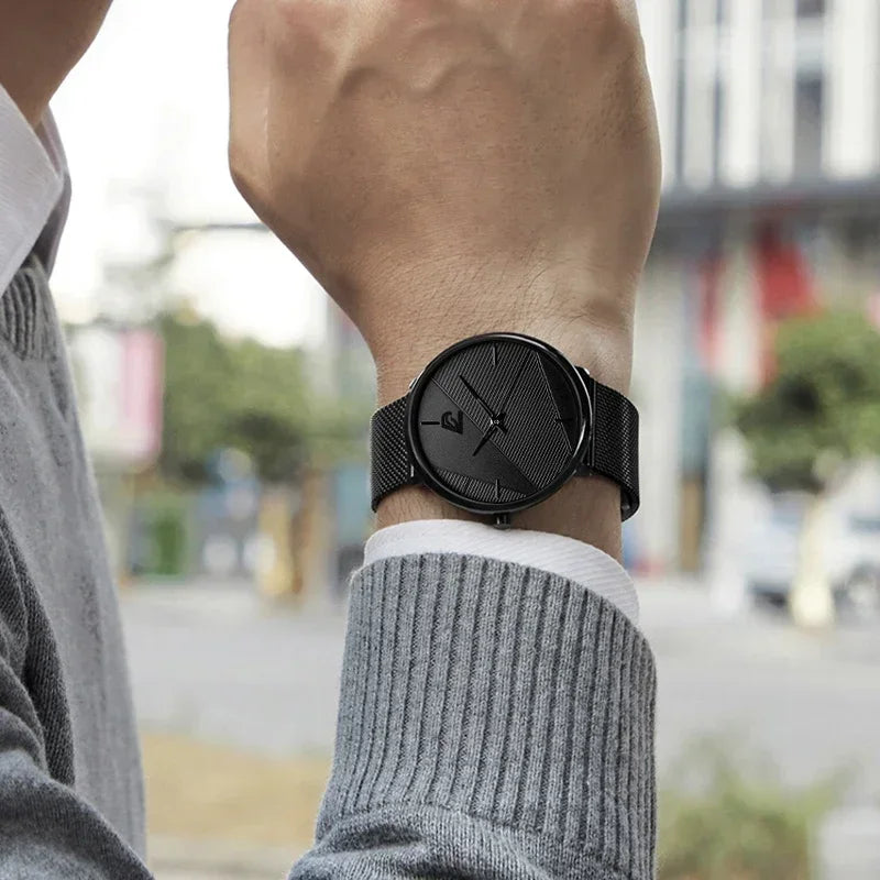 Minimalist men’s ultra-thin quartz watch with a textured black dial and matching black mesh strap on a wrist.