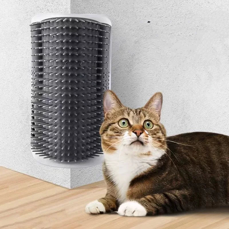 A grey, plastic corner self-grooming brush for cats mounted on a wall with a tabby cat sitting in front.