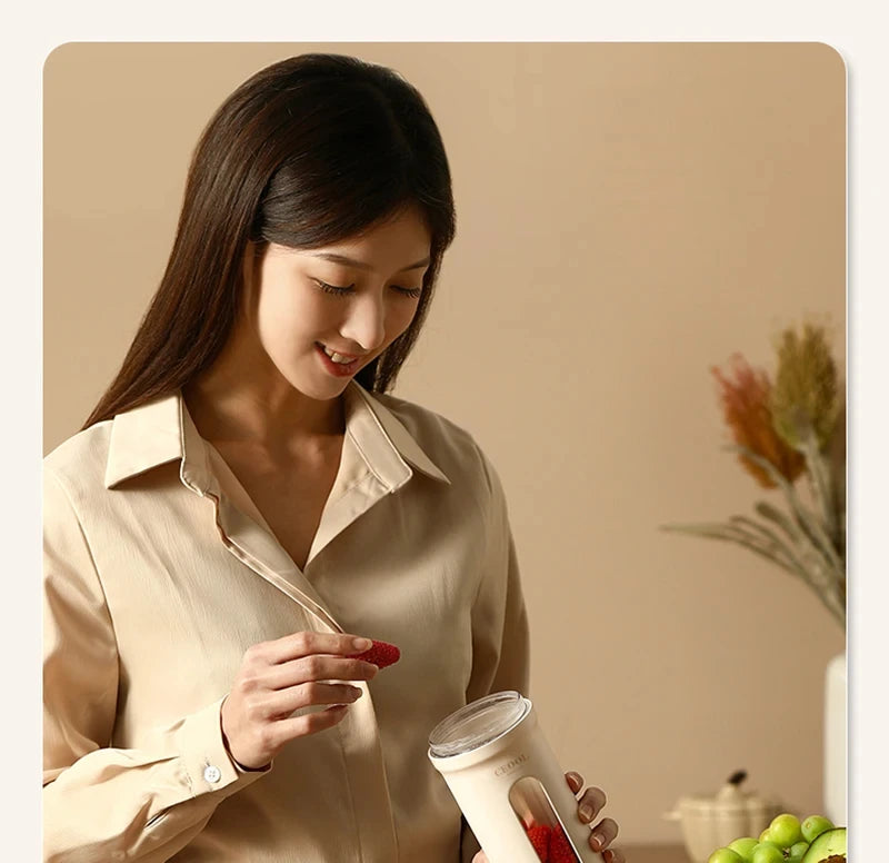 A woman holds a minimalist, beige portable blender while placing a strawberry inside to make a fresh smoothie.