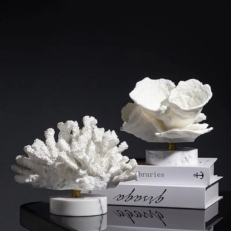 Two white resin coral sculptures on round marble bases, displayed on stacked books against a dark background.