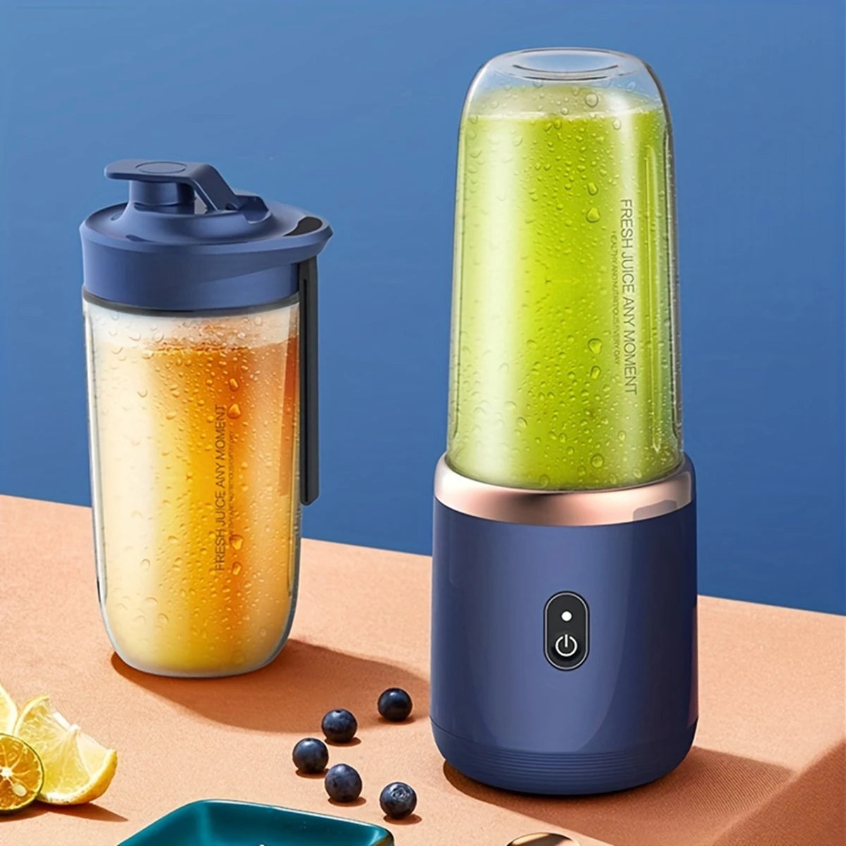 Two portable blue blenders on a table, one containing green juice and the other an orange beverage with fruit nearby.