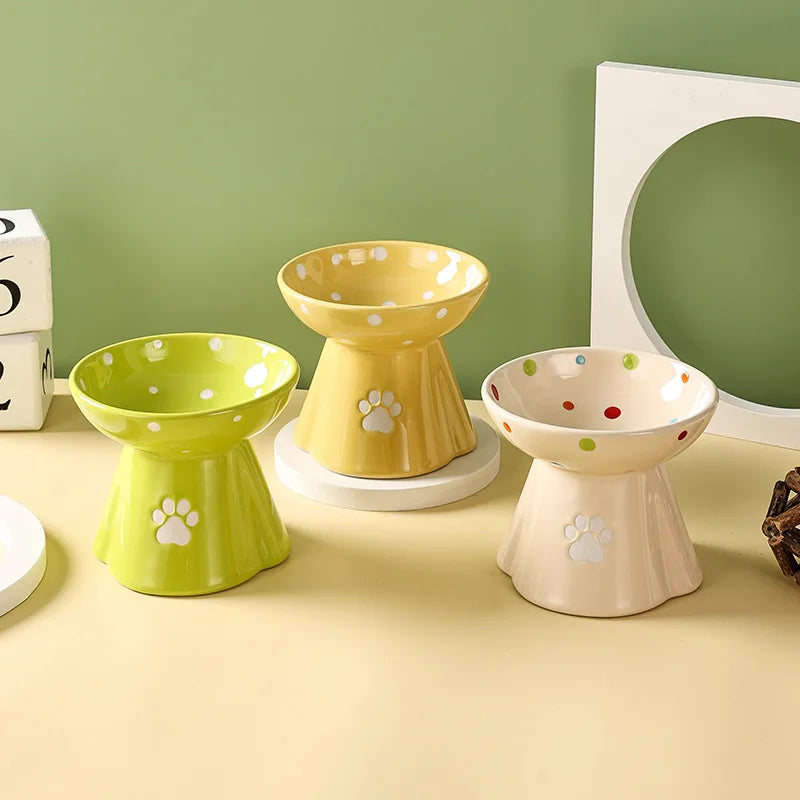 Three elevated, ceramic cat bowls in lime, yellow, and cream, each featuring a paw print and cute polka dot design.