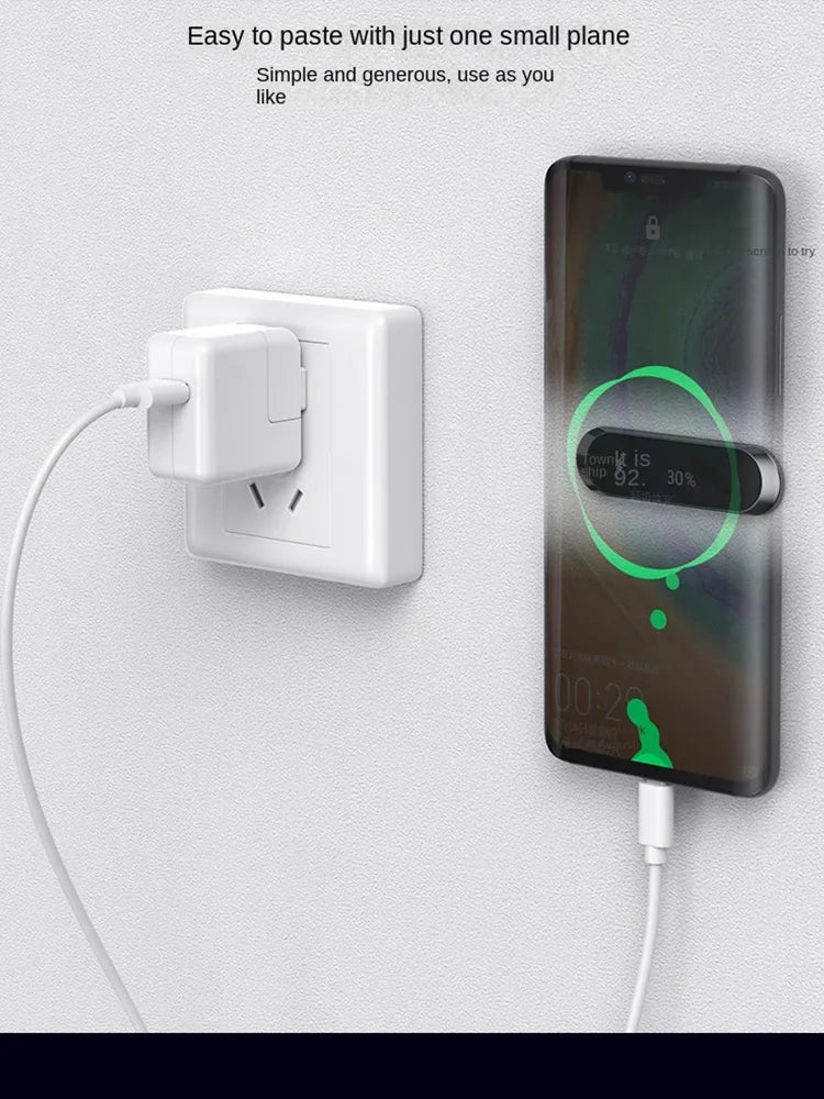 A black smartphone mounted to a wall using a slim, horizontal magnetic adhesive holder, charging via a white cable.