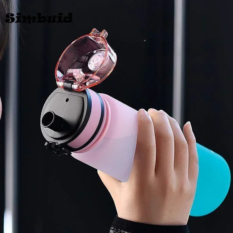 A person holding a translucent pink and blue reusable water bottle with a black flip-top straw lid.