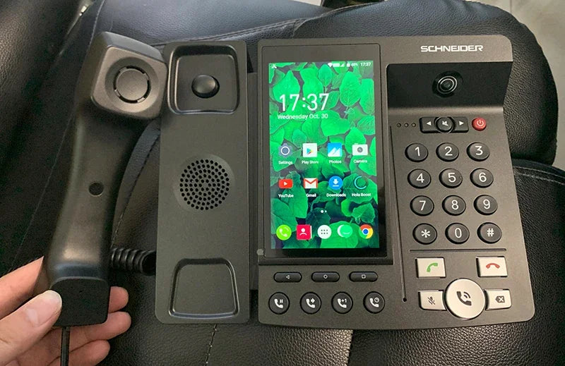Black smart desk phone with a vertical touchscreen interface, physical keypad, and a handset.