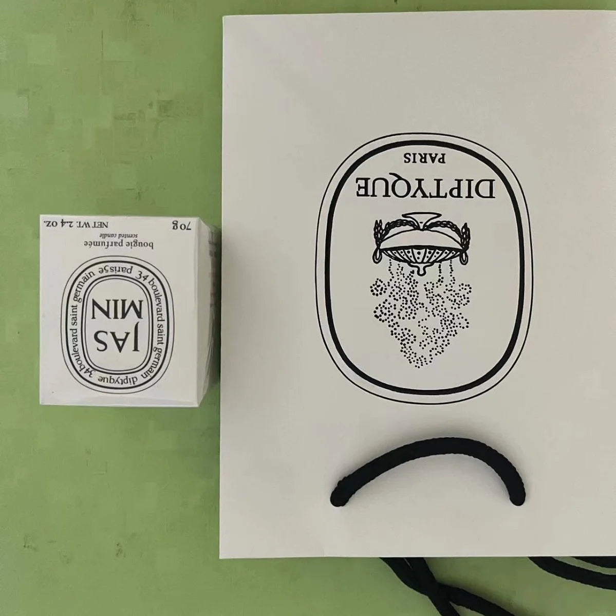 A white 70g scented candle box next to a matching white paper gift bag with black logo and handle.