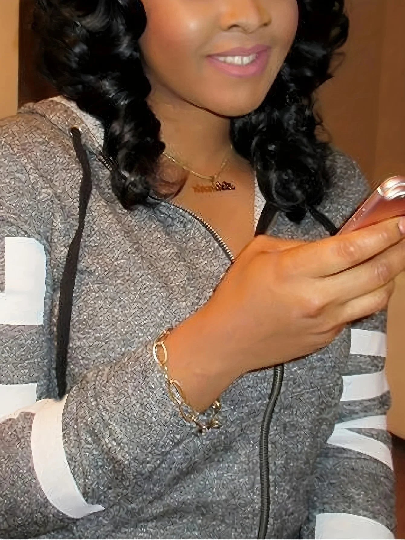 Woman wearing a grey marl zip-up hoodie with white sleeve stripes, gold chain necklace, and a chunky gold link bracelet.