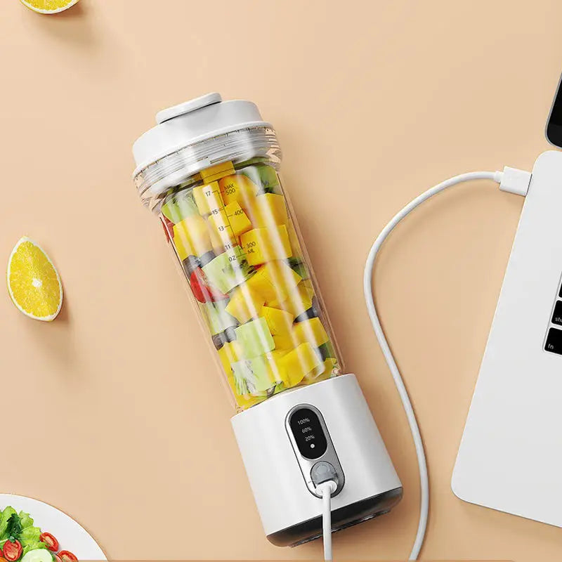 Portable white blender filled with chopped fruit, charging via USB cable on a light beige background.
