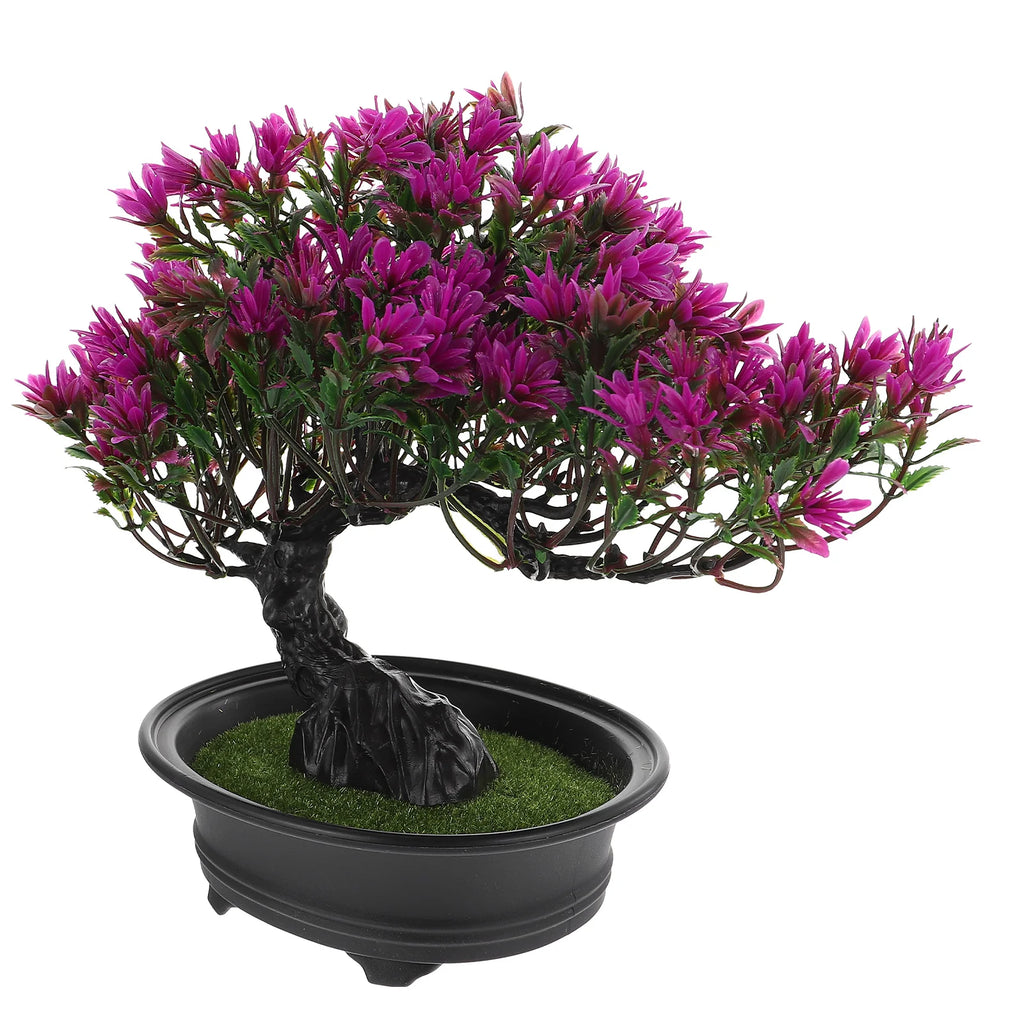 Artificial bonsai tree with vibrant purple flowers in a black oval pot with faux green grass, isolated on white.