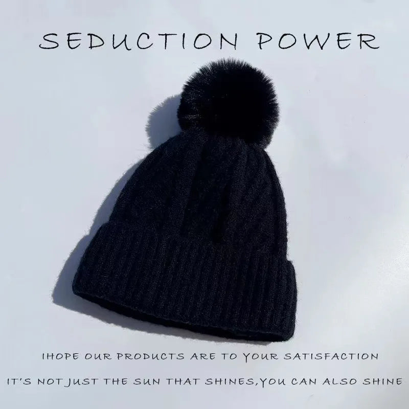 Black knitted winter beanie with a cable knit texture and matching fluffy pom pom on top.