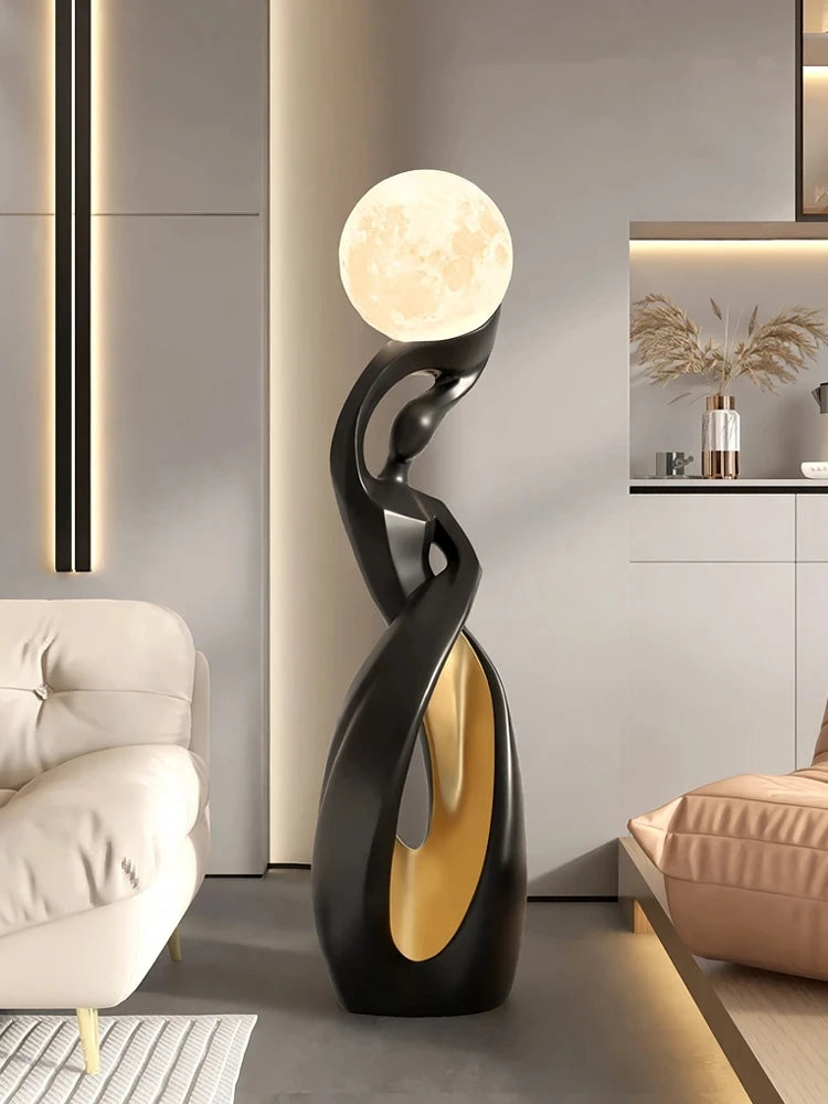 Abstract black and gold resin floor statue featuring an elegant, curved silhouette topped with a glowing moon lamp.
