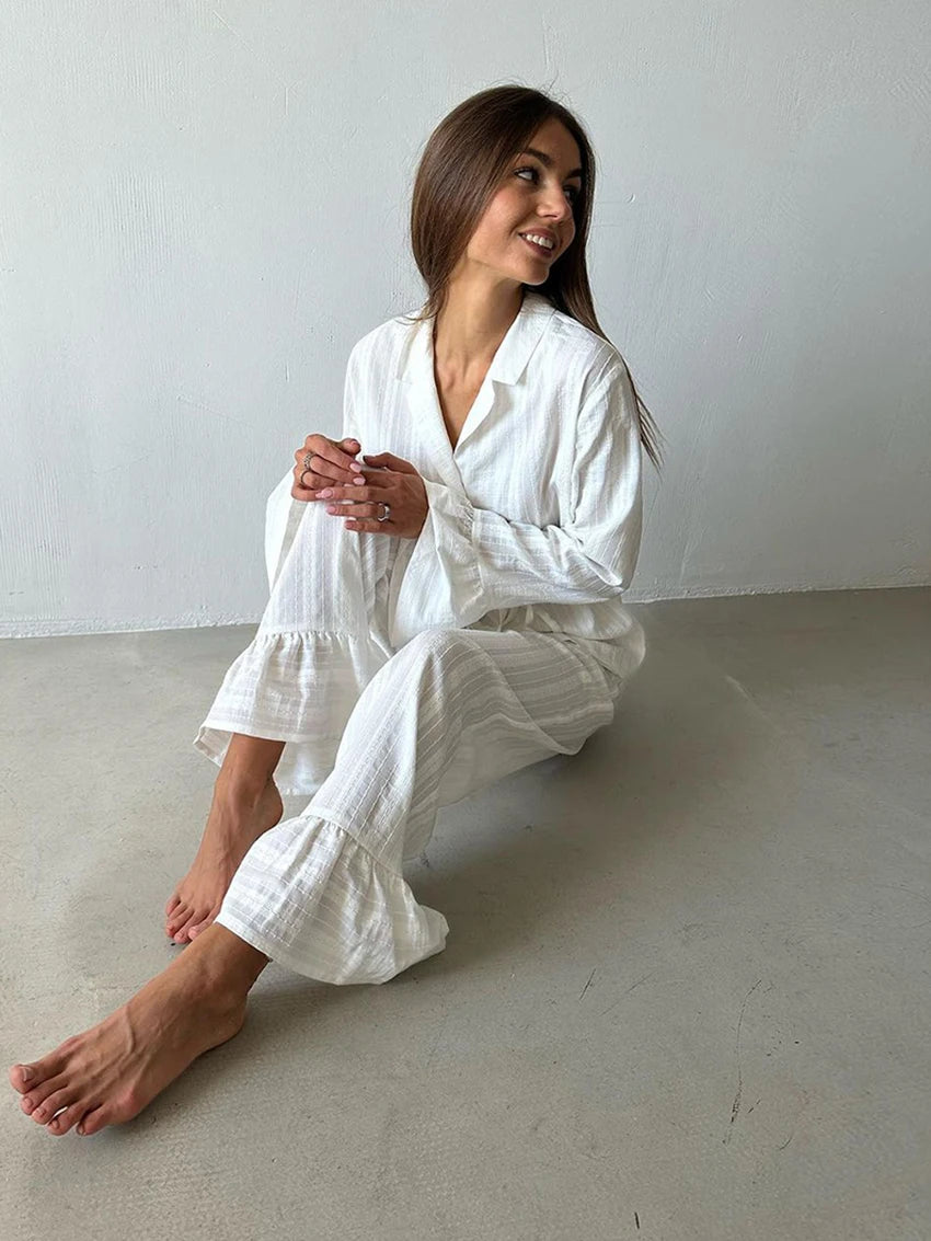 Woman wearing a white, textured, long-sleeved lounge set with ruffled hem detailing on the trousers.