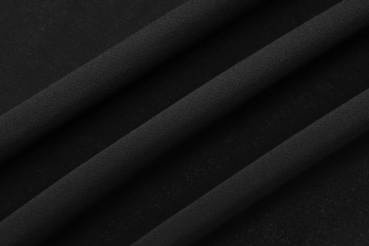 Solid black fabric with a fine, grainy texture and soft, diagonal draped folds.