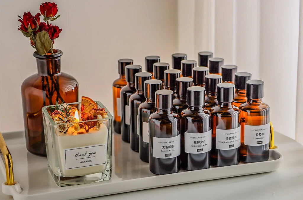 A collection of amber glass essential oil bottles and a "thank you" candle with dried florals on a white tray.