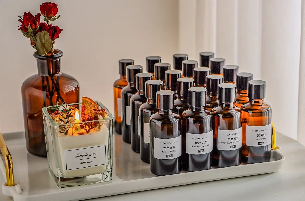 A collection of amber glass essential oil bottles and a "thank you" candle with dried florals on a white tray.
