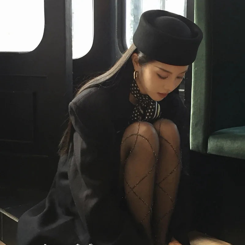 Elegant black wool Hepburn-style bucket hat with a flat crown and structured brim, worn by a woman in a smart outfit.