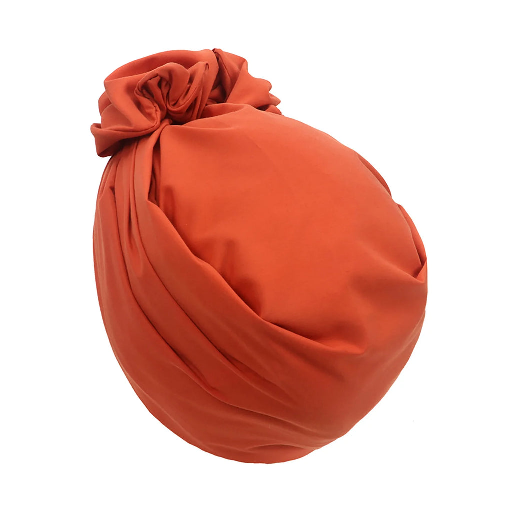 A rust-orange vintage-style turban hat with a gathered, knotted top detail and soft, pleated fabric finish.