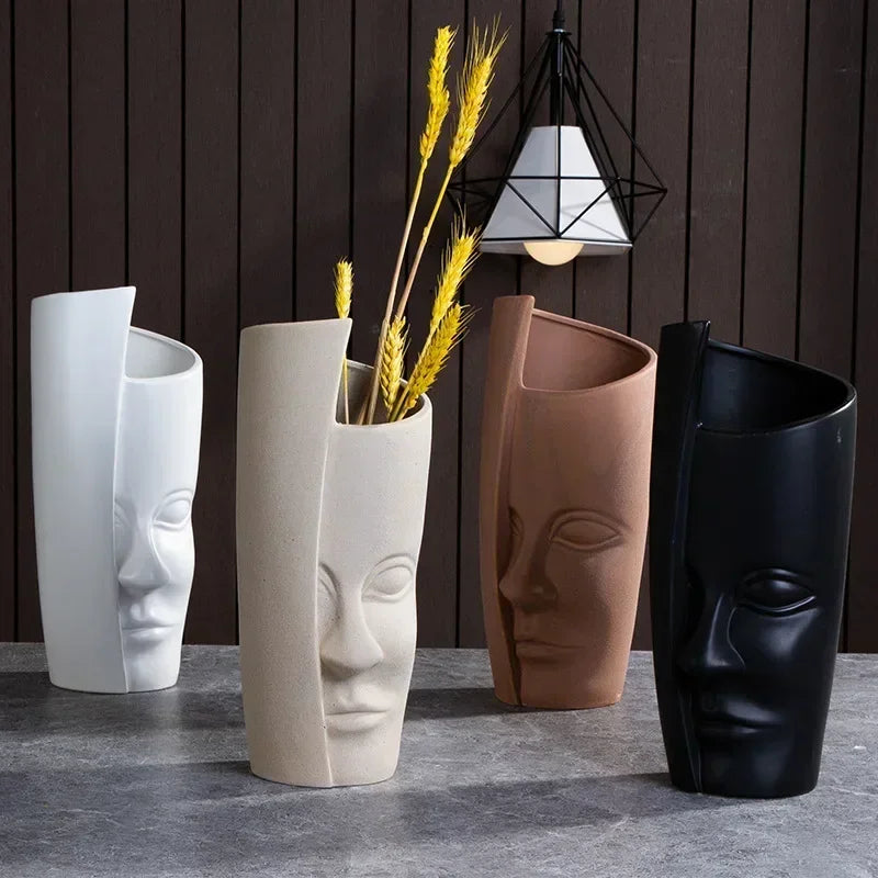 Four abstract face-shaped vases in white, beige, brown, and black, displayed on a grey stone surface.