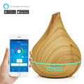 Teardrop-shaped light wood grain essential oil diffuser with a glowing blue LED ring and app control on a smartphone.