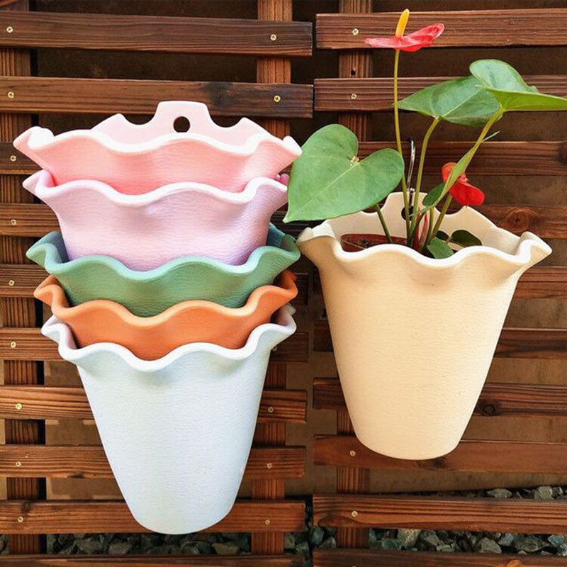 Stacked pastel plastic wall planters with scalloped rims, with one cream pot holding a red-flowered plant on a fence.