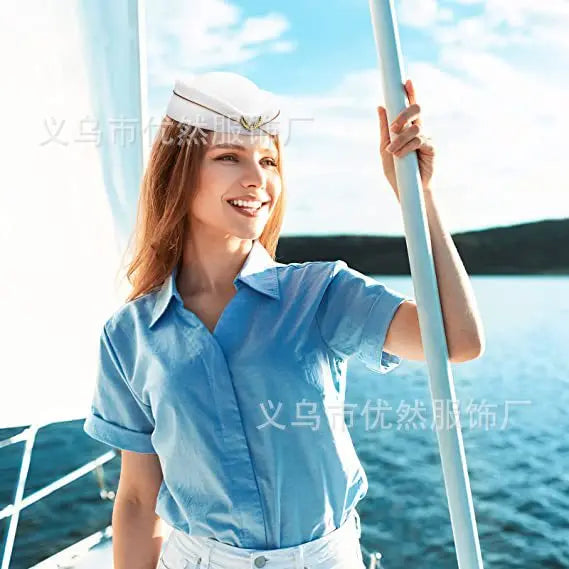 White vintage-style pillbox hat with a thin gold trim and decorative front emblem, worn by a woman on a boat.