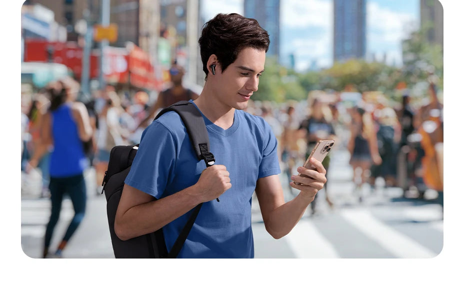 Young man in a blue t-shirt and backpack wearing sleek black wireless earbuds while looking at his smartphone outdoors.