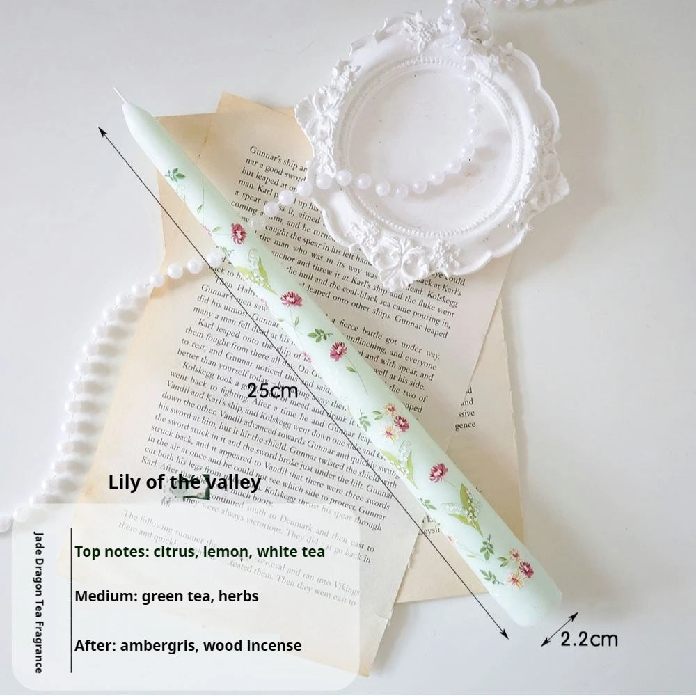 Pale green tapered candle, 25cm tall, featuring delicate floral prints, presented on vintage paper with pearl decor.
