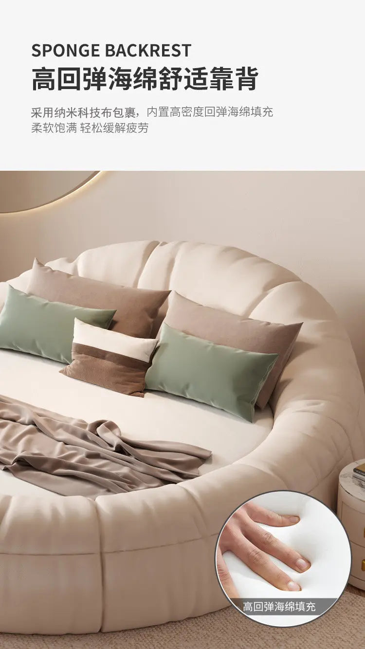 Modern cream-coloured round bed frame with a plush, cushioned sponge backrest, accented with sage and brown pillows.