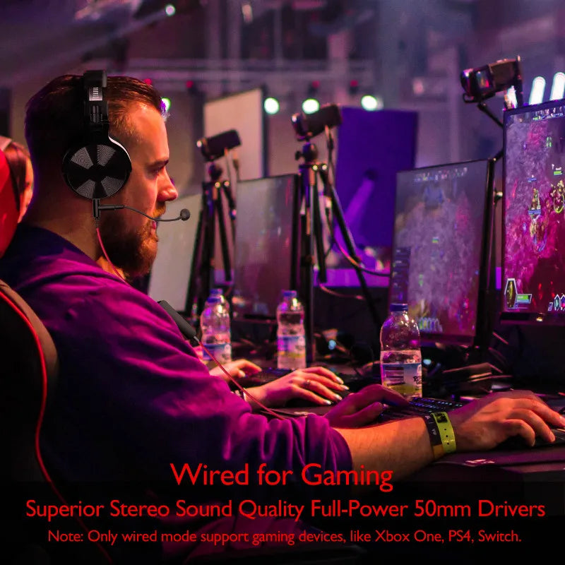 Black over-ear gaming headphones with a boom microphone, worn by a man playing on a computer in a purple-lit room.