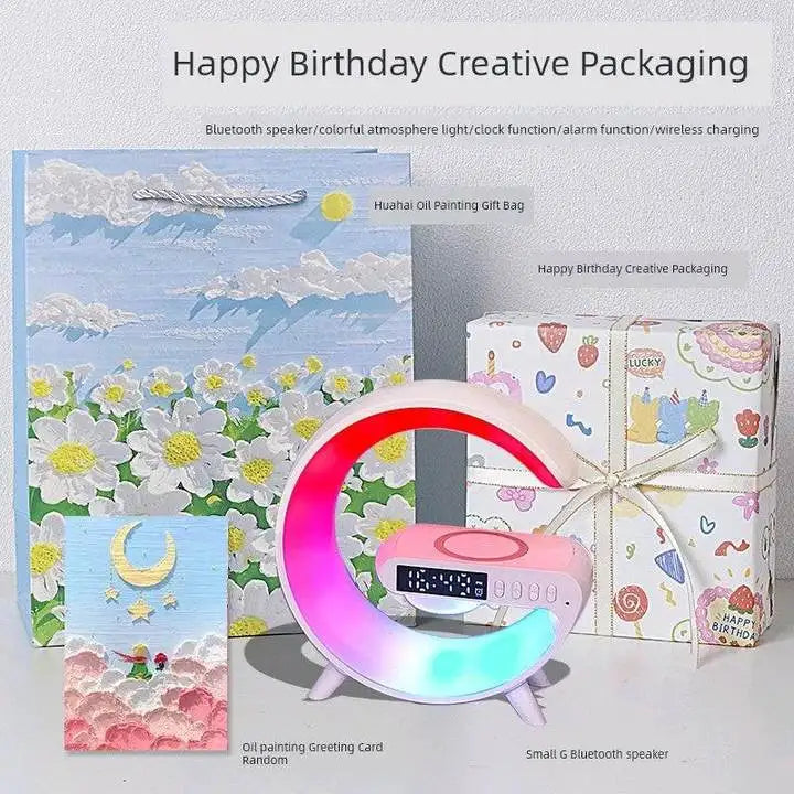 Pink G-shaped Bluetooth speaker with RGB light, digital clock, and wireless charging pad, shown with gift packaging.