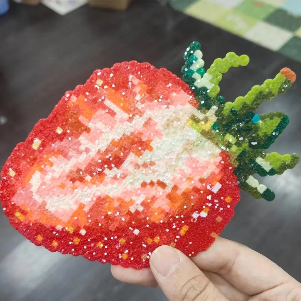 A hand holds a sparkly, pixel-art style strawberry ornament crafted from red, white, and green plastic beads.