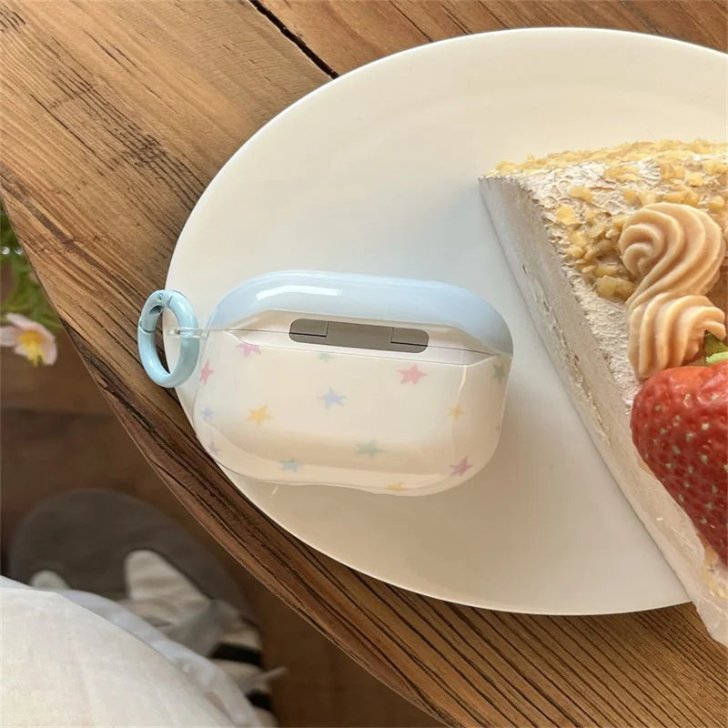 Glossy white AirPods Pro case featuring pastel stars, blue trim, and matching carabiner ring on a plate with cake.