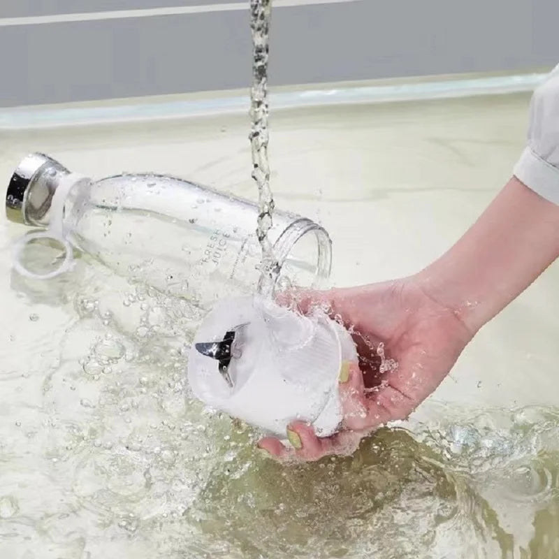 A person rinsing a portable, white, minimalist electric blender and clear bottle under a running water tap.