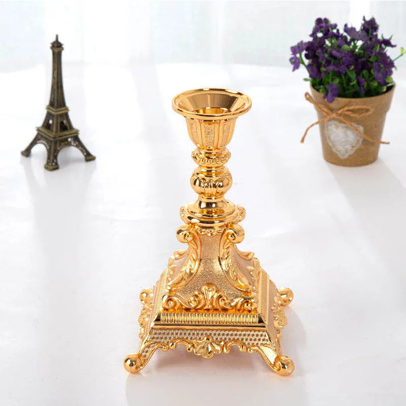 Shiny gold metal candlestick with an ornate, textured square base and decorative pedestal stem.