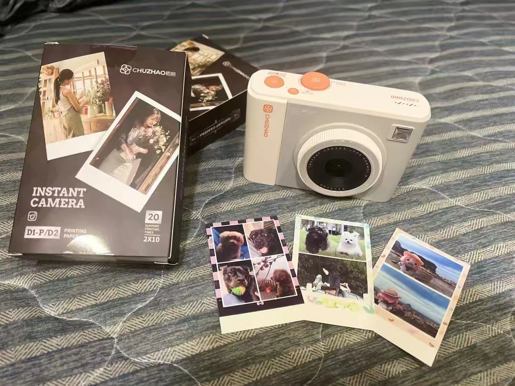 White CHUZHAO instant camera with its box and three printed photos of dogs and scenery on a blue patterned surface.