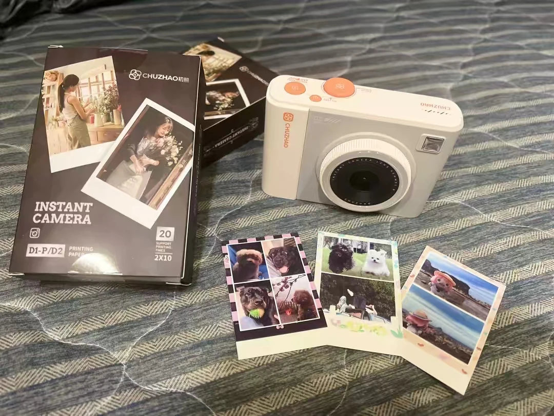 White CHUZHAO instant camera with its box and three printed photos of dogs and scenery on a blue patterned surface.