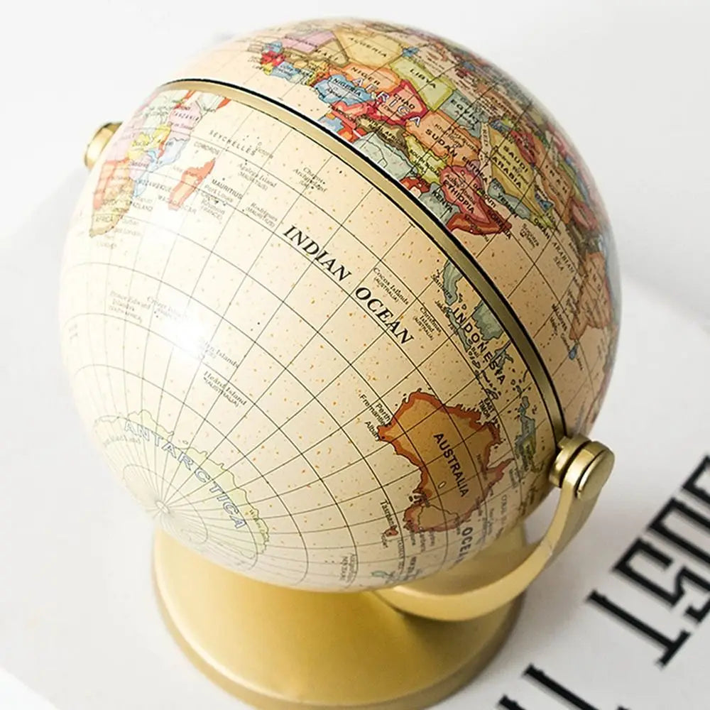 Vintage-style world globe in muted cream and gold tones, featuring a classic stand and detailed map, on a white base.