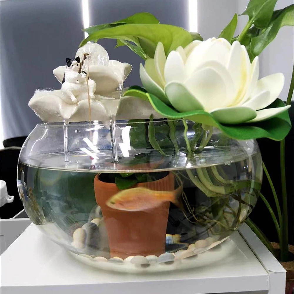 A cute black and white cat ornament fishing on a white lotus-shaped fountain topper, sitting atop a glass fish bowl.