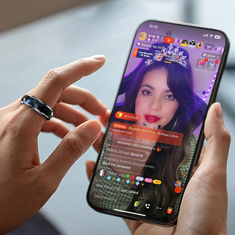 Sleek black smart health ring on a finger, worn while holding a smartphone displaying a social media live stream.