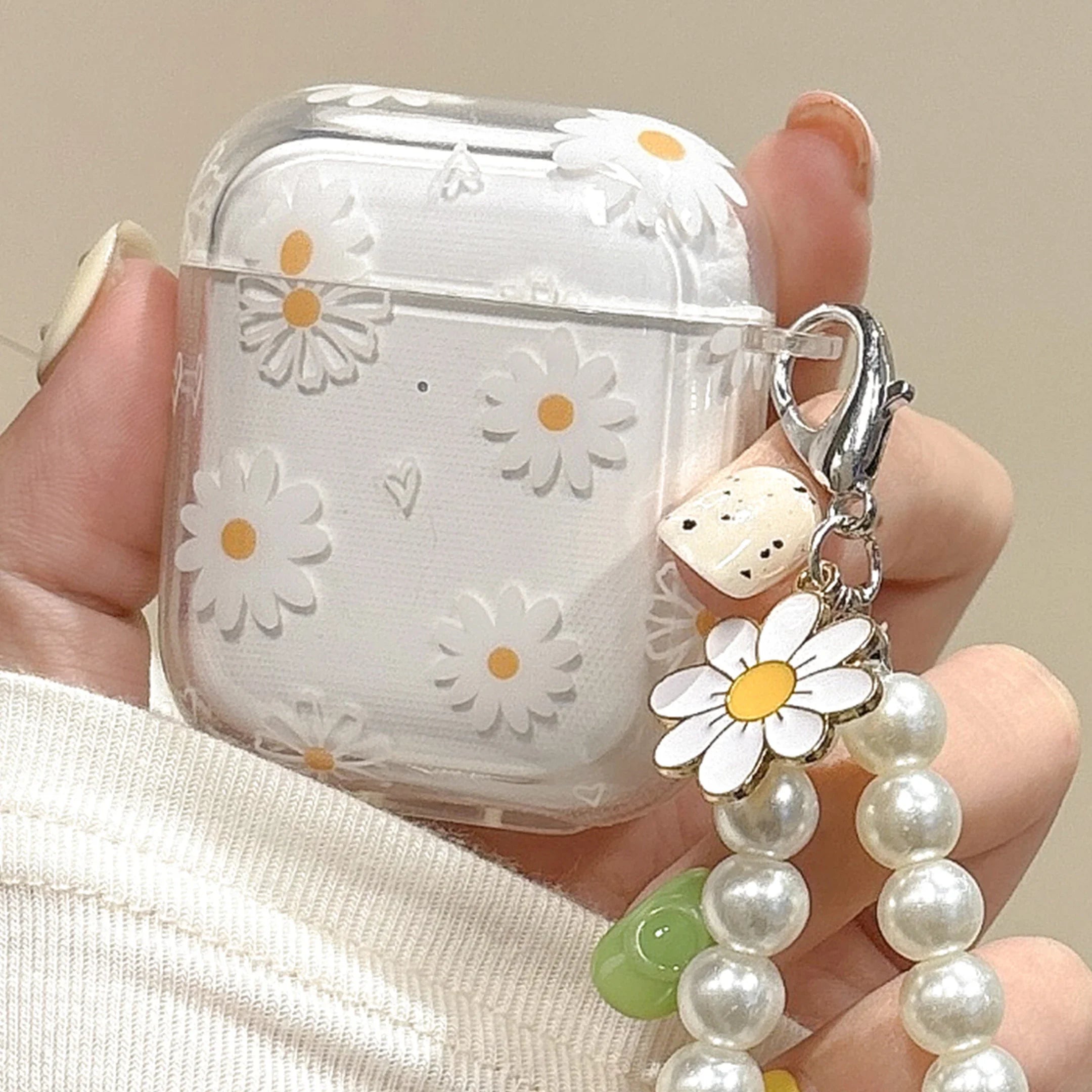 Clear AirPods case with white daisy pattern and pearl charm attachment, suitable for Apple AirPods.