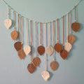 Boho macrame wall hanging featuring cream and brown leaf-shaped tassels accented with wooden beads on a string.