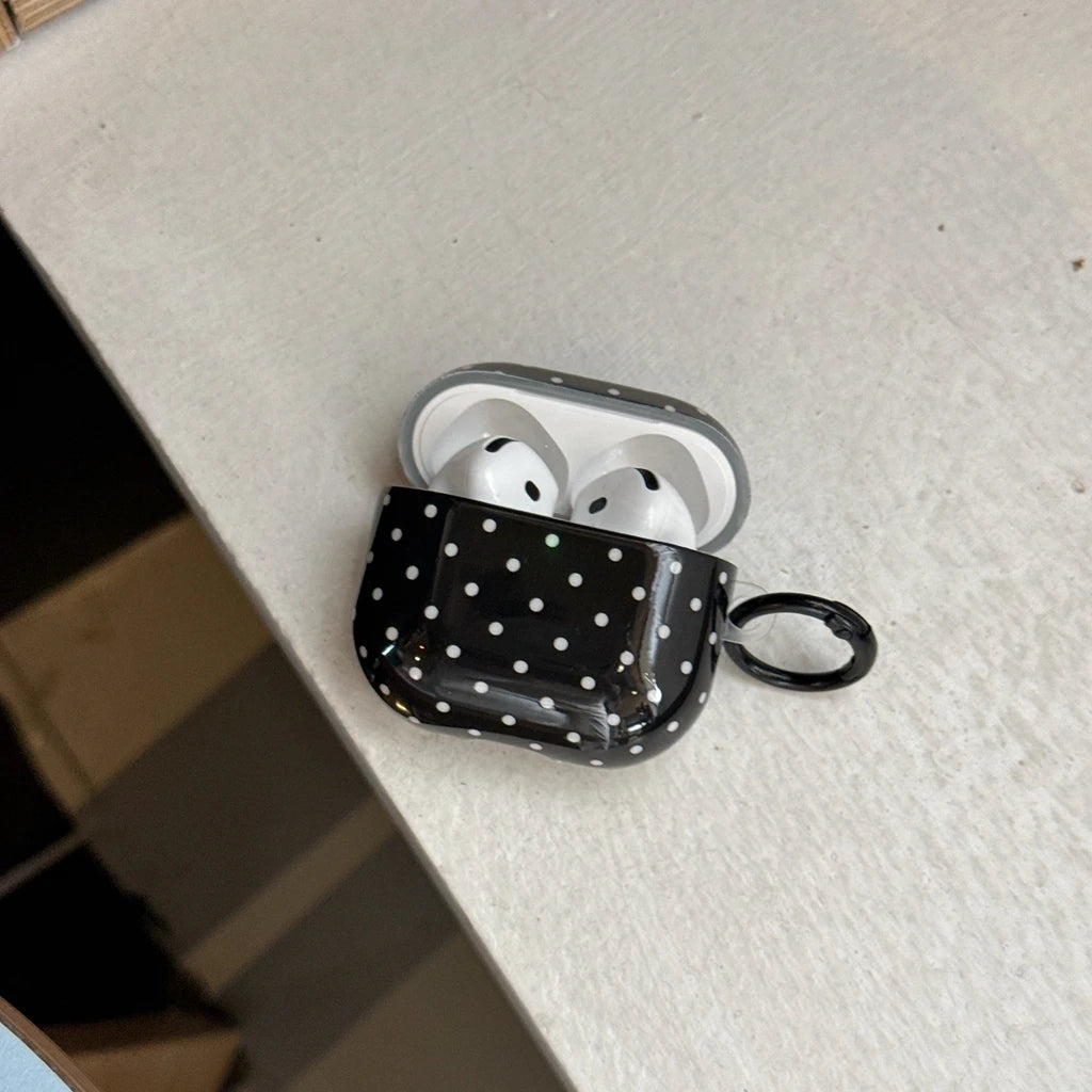 Glossy black and white polka dot silicone AirPods Pro case with carabiner clip on a white surface.
