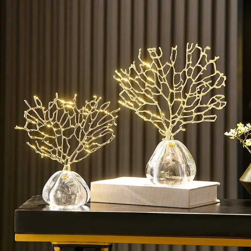 Two decorative gold coral branches with embedded lights in glass bases sit on a black table.